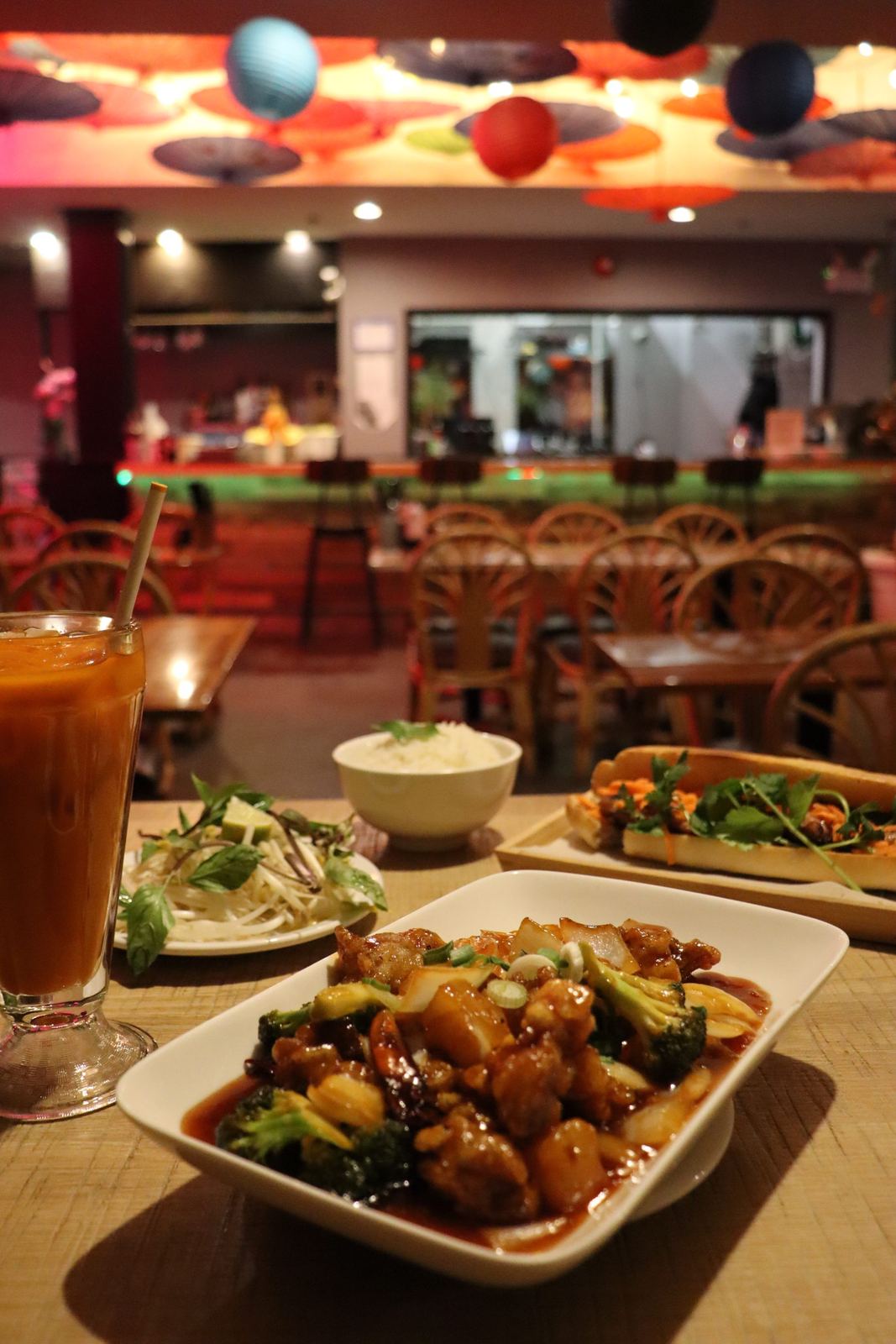 Stir-fried chicken with broccoli, a banh mi, herbs and a Thai iced tea on a table in the dining room
